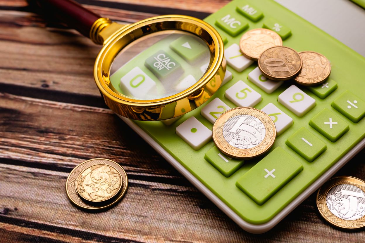 Imagem ilustrativa do post sobre DAS Simples nacional com uma calculadora em close, moedas e uma lupa