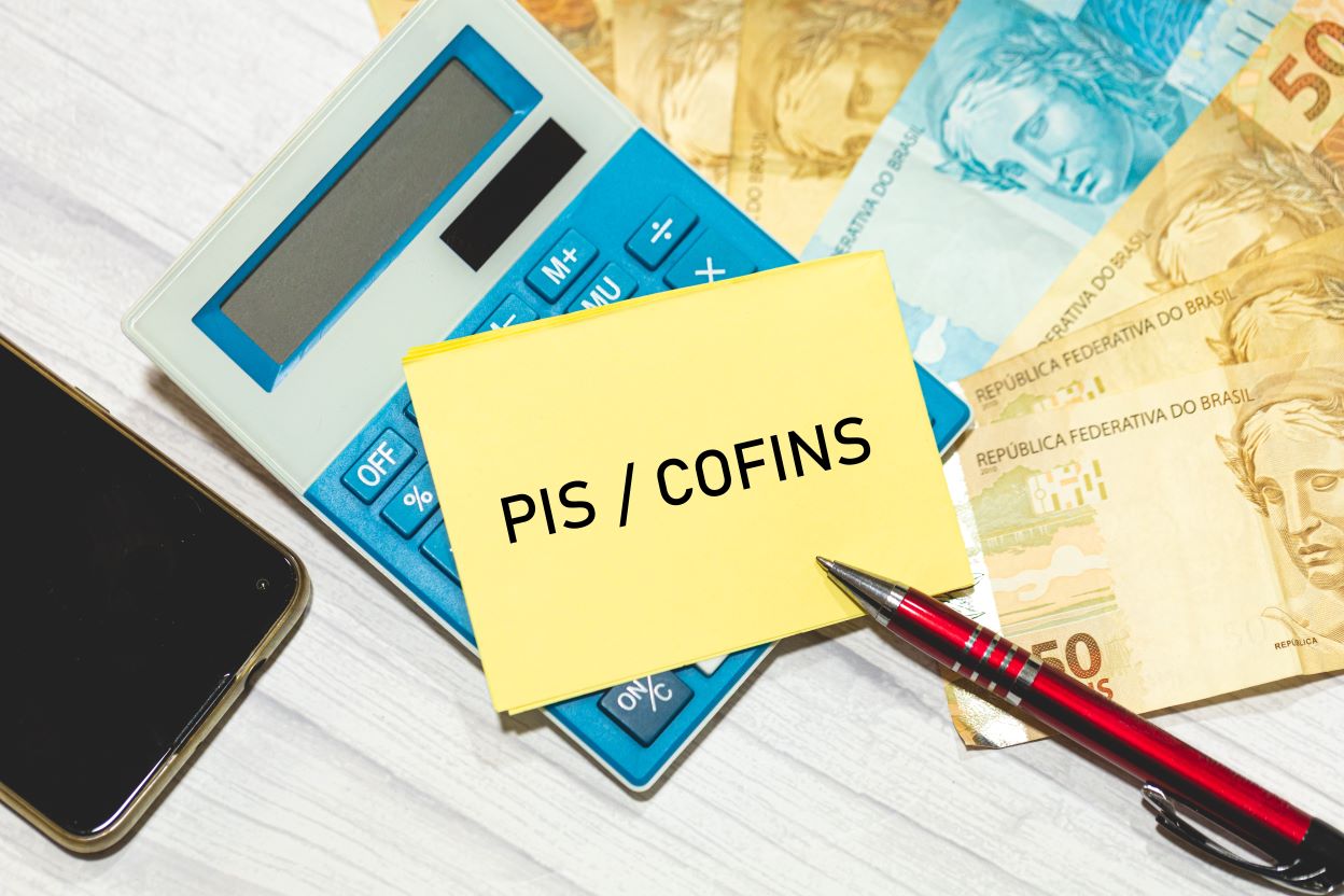 imagem ilustrativa do pis cofins com notas de dinheiro, calculadora e caneta